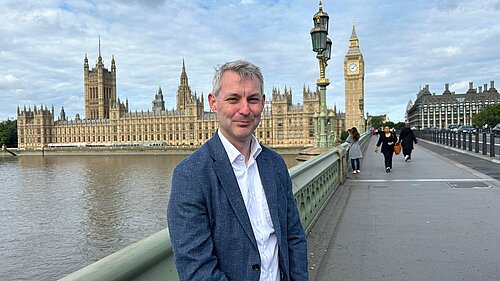 Will Forster with view of Houses of Parliament behind him